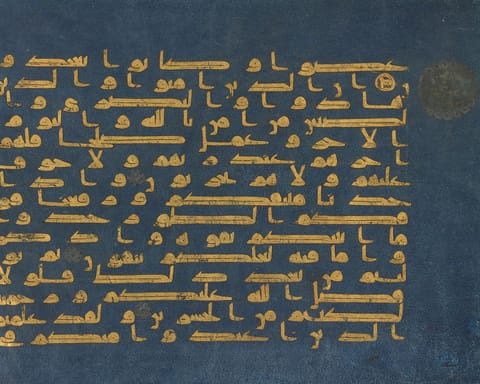 Gold Kufic letters in long horizontal strokes on parchment dyed deep indigo, with a small gold verse marker at the right edge.