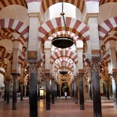 Rows of double-tiered horseshoe arches striped in red brick and white stone march away on slender columns through the dim prayer hall of the Great Mosque of Córdoba.