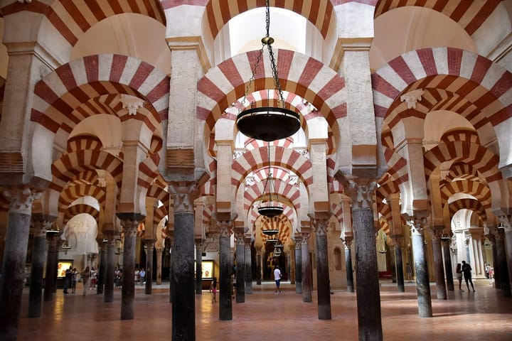 Rows of double-tiered horseshoe arches striped in red brick and white stone march away on slender columns through the dim prayer hall of the Great Mosque of Córdoba.