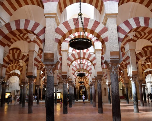 Rows of double-tiered horseshoe arches striped in red brick and white stone march away on slender columns through the dim prayer hall of the Great Mosque of Córdoba.