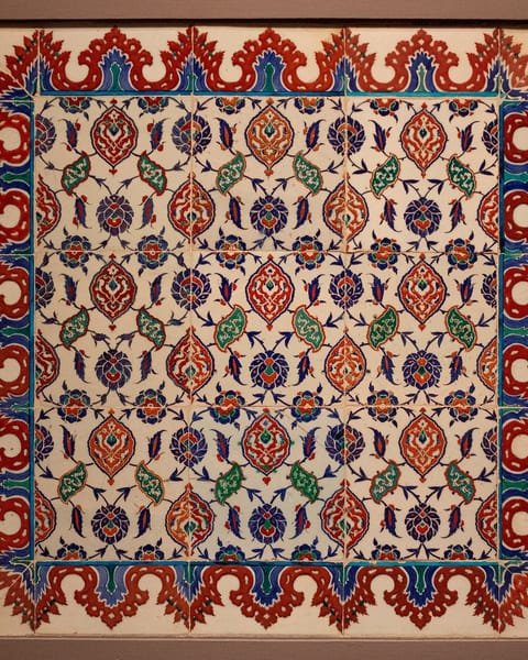 A square panel of white Iznik tiles patterned with red, cobalt, and green flowers and leaves inside a scalloped red border.