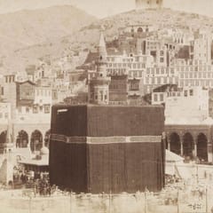 An early sepia photograph of the Kaaba in its black cloth cover inside the arcaded courtyard of the Great Mosque of Mecca, with the houses of the city climbing the hills behind.