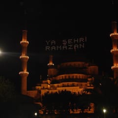 The domes and minarets of the Blue Mosque glow against the night sky, with the words “Ya Şehr-i Ramazan” (O month of Ramadan) spelled in lights between the minarets.