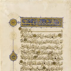 A cream page of flowing gold script outlined in black, with gold verse rosettes, a blue and gold heading panel, and round gold medallions in the margin.