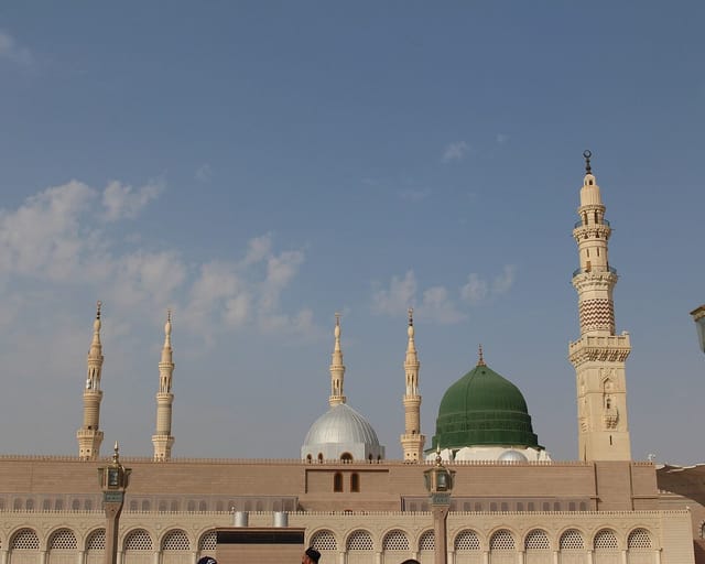The green dome over the Prophet's resting place rises beside a silver dome and tall white minarets above the arcades of the mosque in Medina.