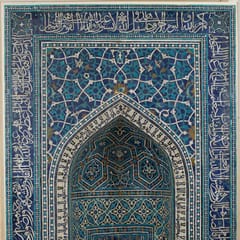 A tall prayer niche in turquoise, cobalt, and white tile mosaic, framed by bands of Quranic inscription with a pointed arch at its heart.
