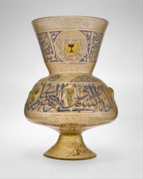 A tall enameled glass lamp with a flared neck, its body ringed with large blue Arabic letters and a red and gold emblem.