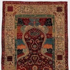 A silk and wool prayer rug with an arched niche filled with red flowering vines, framed by wide borders of woven inscription.