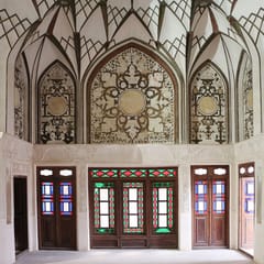 A white reception room with carved stucco vaults and wooden doors set with small panes of red, blue, and green glass.