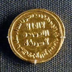 A gold coin on dark cloth with Arabic inscriptions in plain Kufic letters across its face and around its rim.