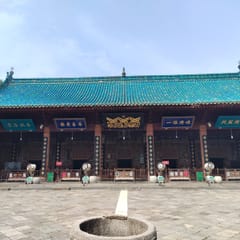 A Chinese-style prayer hall with a sweeping turquoise-tiled roof, red columns, and blue-and-gold signboards under the eaves, fronted by a paved stone courtyard.